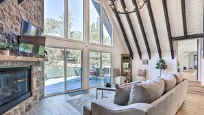 Un salón amplio con chimenea de piedra, ventanas grandes y un techo alto con vigas a la vista.