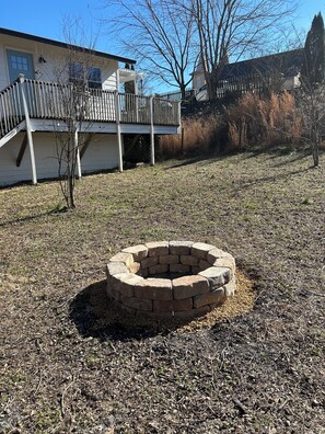 A backyard with a stone fire pit, a wooden deck, and a house with a light blue door.