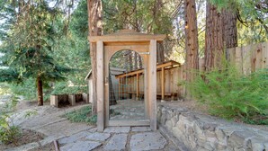 Un vialetto in pietra conduce a un gazebo in legno con cancello in metallo, circondato da alberi e da un recinto in legno.