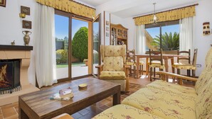 A living room with a fireplace, a sofa, a coffee table with books, and a dining area with chairs and a table. - 2CIP01-10pax - House with capacity for 10 people and private pool located in a quiet area (Vidreres)