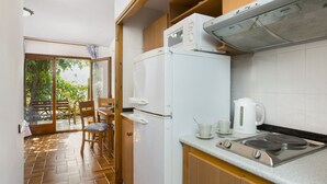 A compact kitchen with a refrigerator, stove, and kettle. There is a dining area with a table and chairs visible through an open door. - 2CIP01-10pax - House with capacity for 10 people and private pool located in a quiet area (Vidreres)
