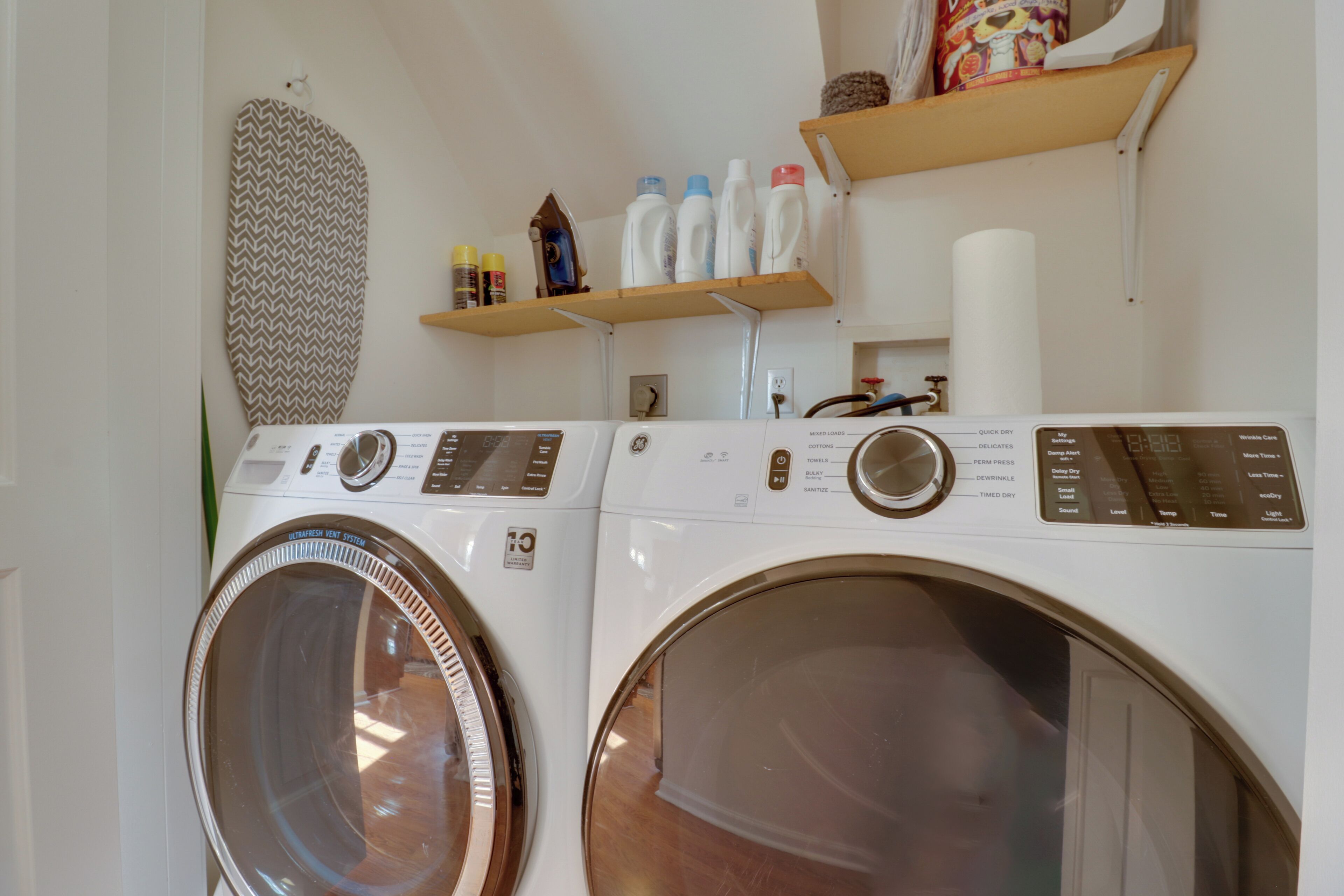 A laundry area with two front-loading washing machines, a patterned wall hanging, and shelves with laundry supplies.