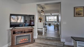 A modern living room with a fireplace, a television, and a dining area with a view of the outdoors.