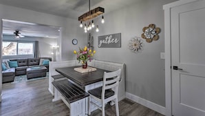 A dining area with a wooden table, white chairs, and a hanging light fixture.
