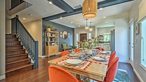 A dining area with a wooden table set for four, surrounded by orange chairs, a staircase, and a bookshelf. - Luxe Lake Arrowhead Farmhouse w/ Deck + Patio (Lake Arrowhead)