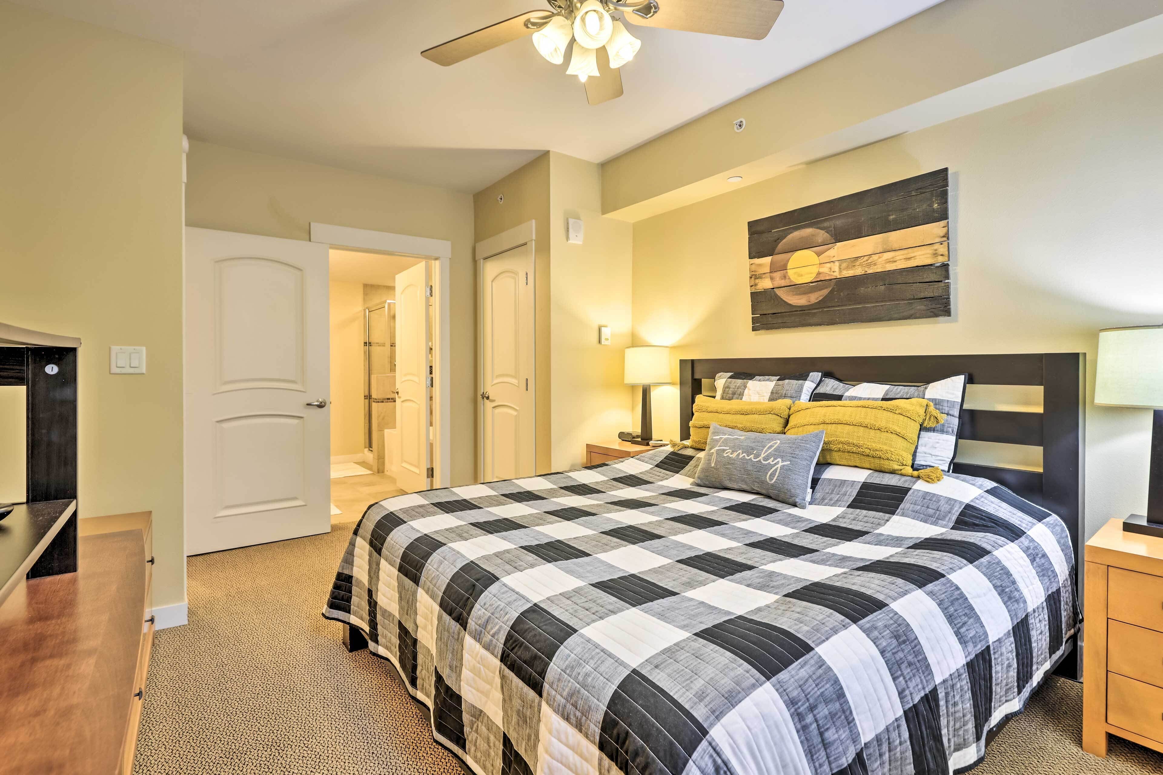 A bedroom with a large bed, a ceiling fan, a wall-mounted artwork, and a door leading to another room.