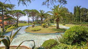 Ein angelegter Garten mit einem klaren Wasserspiel, Palmen und einem Gebäude im Hintergrund.