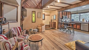 A spacious living area with wooden floors, a kitchen with modern appliances, and a cozy seating area with striped chairs and a round table.