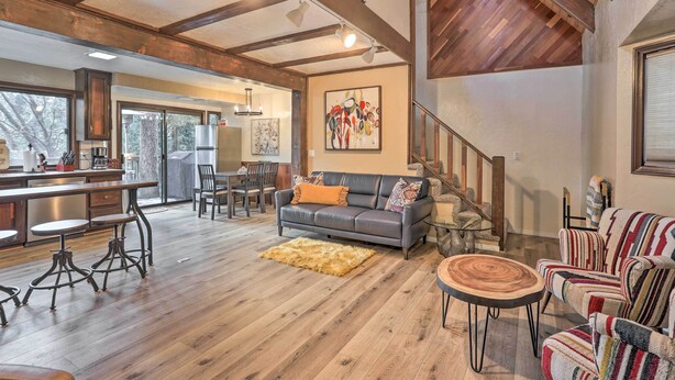A spacious living area with a wooden floor, a leather sofa, striped chairs, a dining table with stools, and a staircase with a wooden railing.