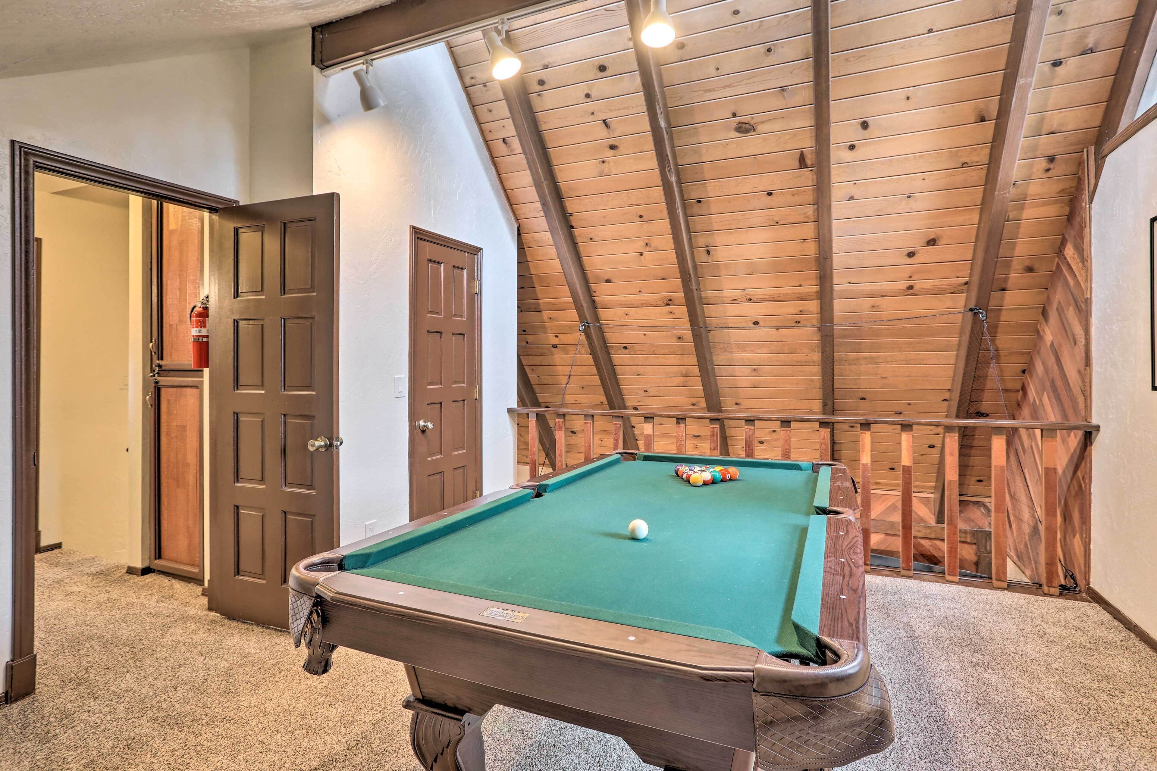 A pool table in a room with a sloped wooden ceiling and a door leading to another room.
