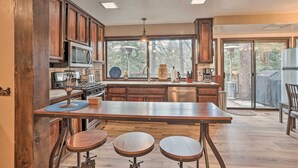 A kitchen with wooden cabinets, a central island with stools, a microwave, and a large window with a view of trees.
