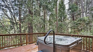 A hot tub on a wooden deck surrounded by a wooden railing, with a view of a forested area.