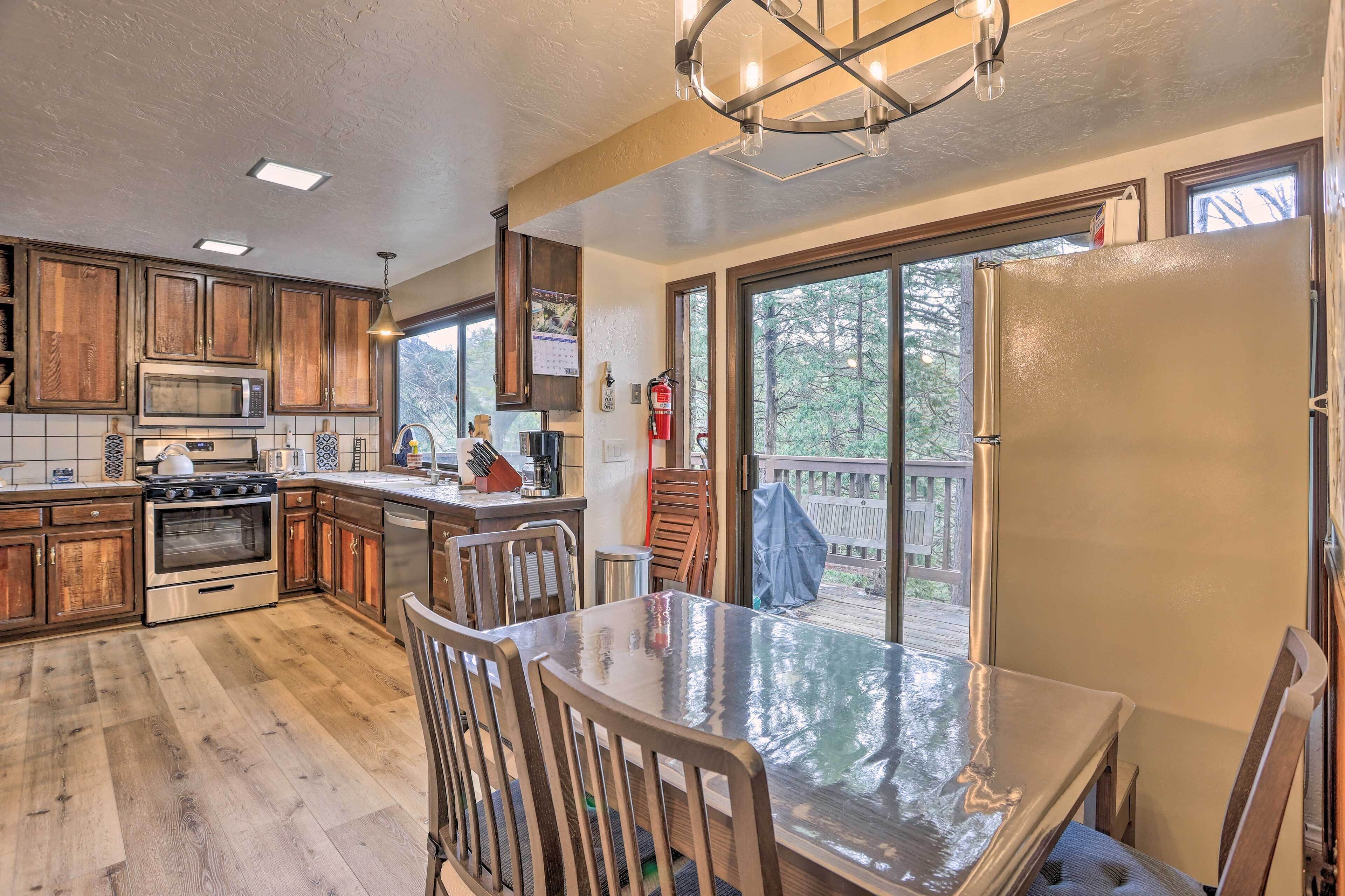 A kitchen with wooden cabinets, a stainless steel refrigerator, a dining table with chairs, and a view of a deck through large windows.