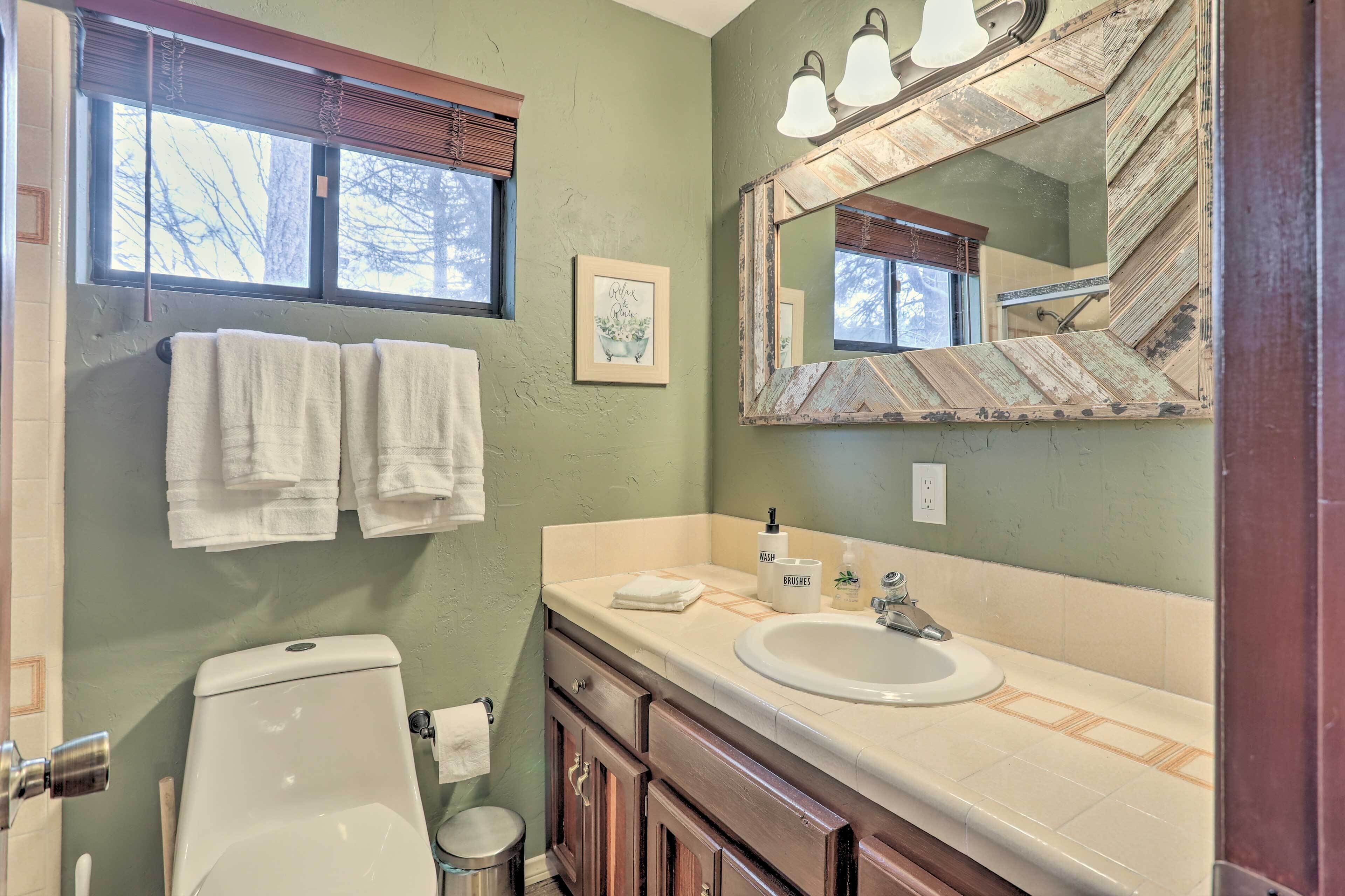 A bathroom with a toilet, sink, and mirror. There are towels hanging on the wall and a framed picture.