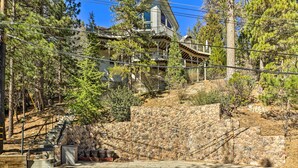 A two-story house with a stone retaining wall, a wooden deck, and a staircase leading to the upper level. - Beautiful Lake Arrowhead Cabin w/ EV Charger (Lake Arrowhead)