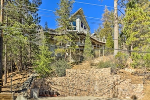 A two-story house with a stone retaining wall, a wooden staircase, and a balcony.