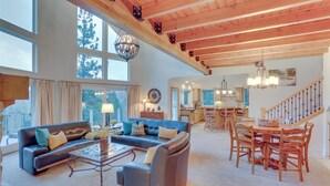 A spacious living room with a large sofa, coffee table, and dining area with wooden chairs. - Beautiful Lake Arrowhead Cabin w/ EV Charger (Lake Arrowhead)