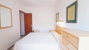 A hotel room with a bed, a wooden dresser, a nightstand, a mirror, and a door.