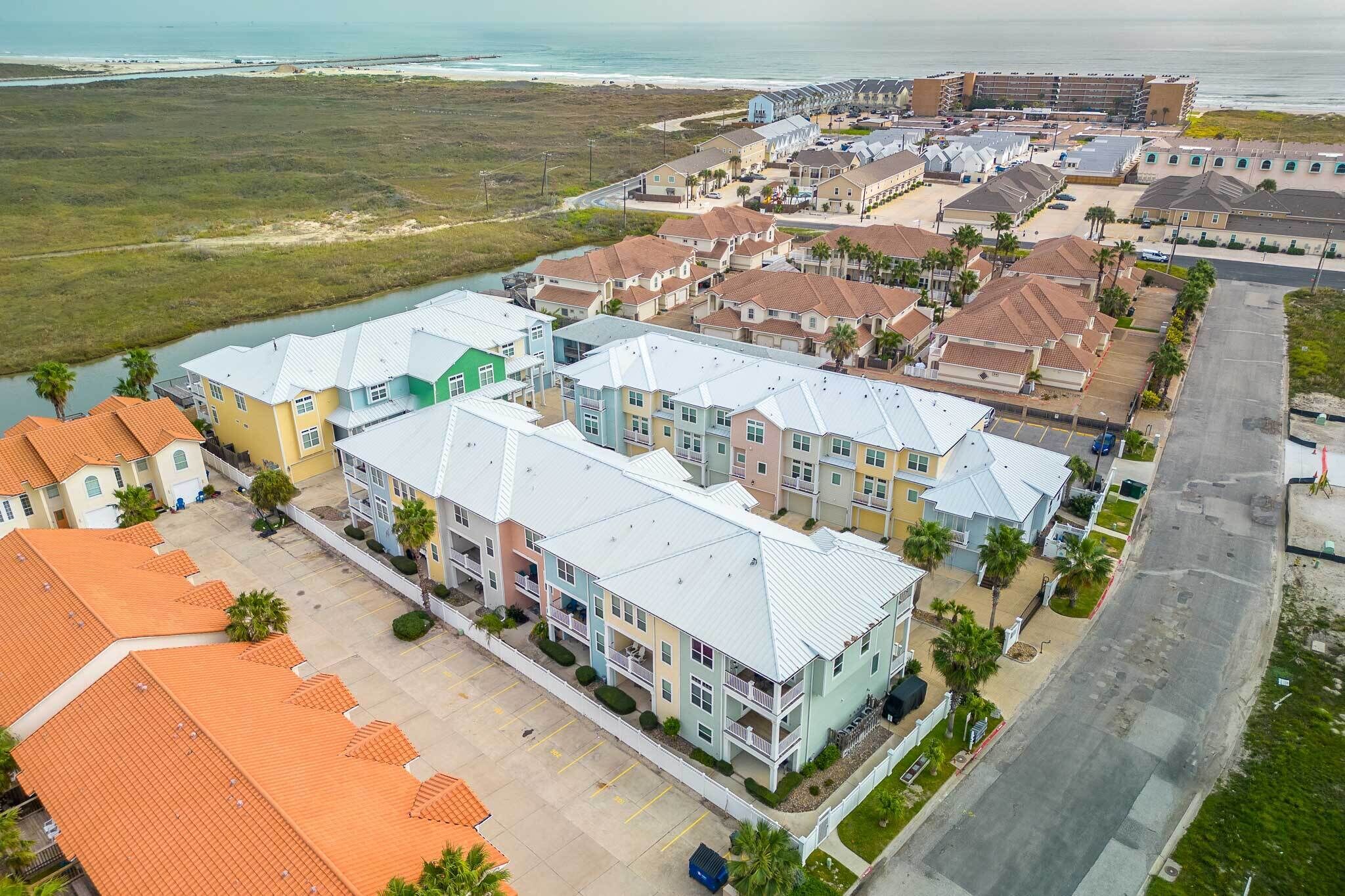 A coastal residential area with a row of townhouses, a parking lot, and a beach in the background.