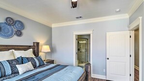 A bedroom with a bed, a nightstand, a lamp, a door, and a shower area. - Corpus Christi Home w/ Golf Cart: Walk to Beach! (Corpus Christi)