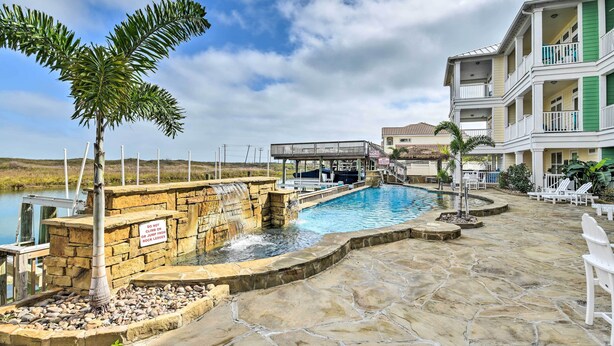 A pool area with a waterfall feature, a palm tree, and a multi-story building with balconies. - Corpus Christi Home w/ Golf Cart: Walk to Beach! (Corpus Christi)