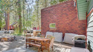 A wooden deck with a table and chairs, a brick wall, and a covered area with appliances. - 1 Mi to Snow Summit: Big Bear Lake Cabin! (Big Bear Lake)