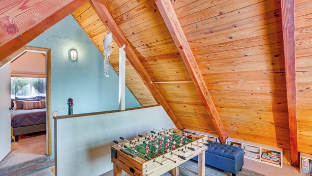 Una habitación acogedora en el ático con techo de madera, mesa de fútbol, sofá azul y estantería.