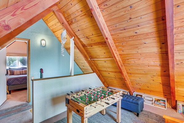 A cozy attic room with a wooden ceiling, a foosball table, a blue sofa, and a bookshelf. - 1 Mi to Snow Summit: Big Bear Lake Cabin! (Big Bear Lake)