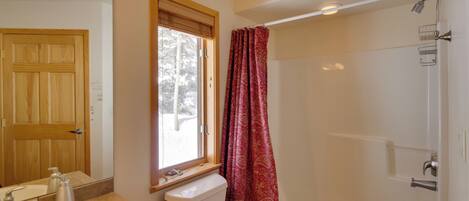 Un baño con puerta de madera, ventana con vistas, inodoro, lavabo y zona de ducha.