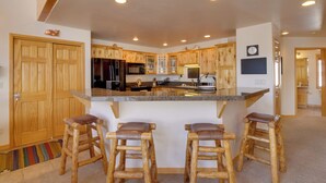 A kitchen with wooden cabinets, a granite countertop, and a built-in island with stools. - Slopeside Sanctuary - Penthouse < 1 Mi to Lifts! (Winter Park)