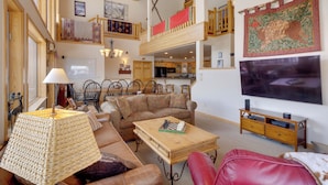 A spacious living room with a high ceiling, a wooden coffee table, a sofa, and a red chair. There is a television on the wall and a small wooden cabinet. - Slopeside Sanctuary - Penthouse < 1 Mi to Lifts! (Winter Park)