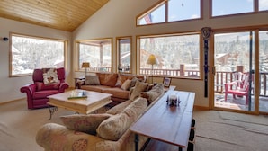 A spacious living room with a high wooden ceiling, large windows offering a view of a snowy landscape, a red leather sofa, a beige sofa, and a wooden coffee table. - Slopeside Sanctuary - Penthouse < 1 Mi to Lifts! (Winter Park)