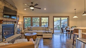 A spacious living room with a stone fireplace, a large flat-screen TV, a ceiling fan, and a dining area with a kitchen counter. - Mountain View Retreat, Walk to Winter Park Gondola (Winter Park)