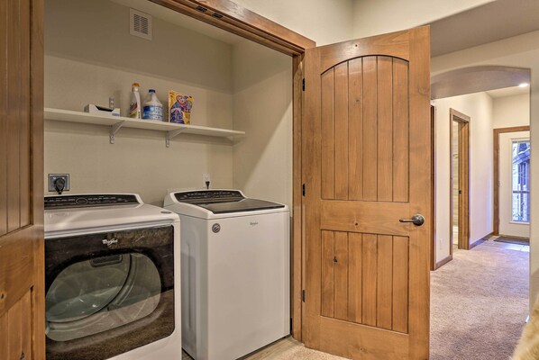 A laundry room with two front-loading washers and dryers, wooden door, and shelves with cleaning supplies. - Mountain View Retreat, Walk to Winter Park Gondola (Winter Park)
