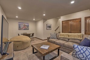 A living room with a sofa, a coffee table, a bean bag, a dining table, and a painting on the wall.