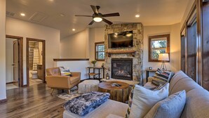 A spacious living room with a stone fireplace, a ceiling fan, and a large flat-screen TV mounted above it. - Mountain View Retreat, Walk to Winter Park Gondola (Winter Park)