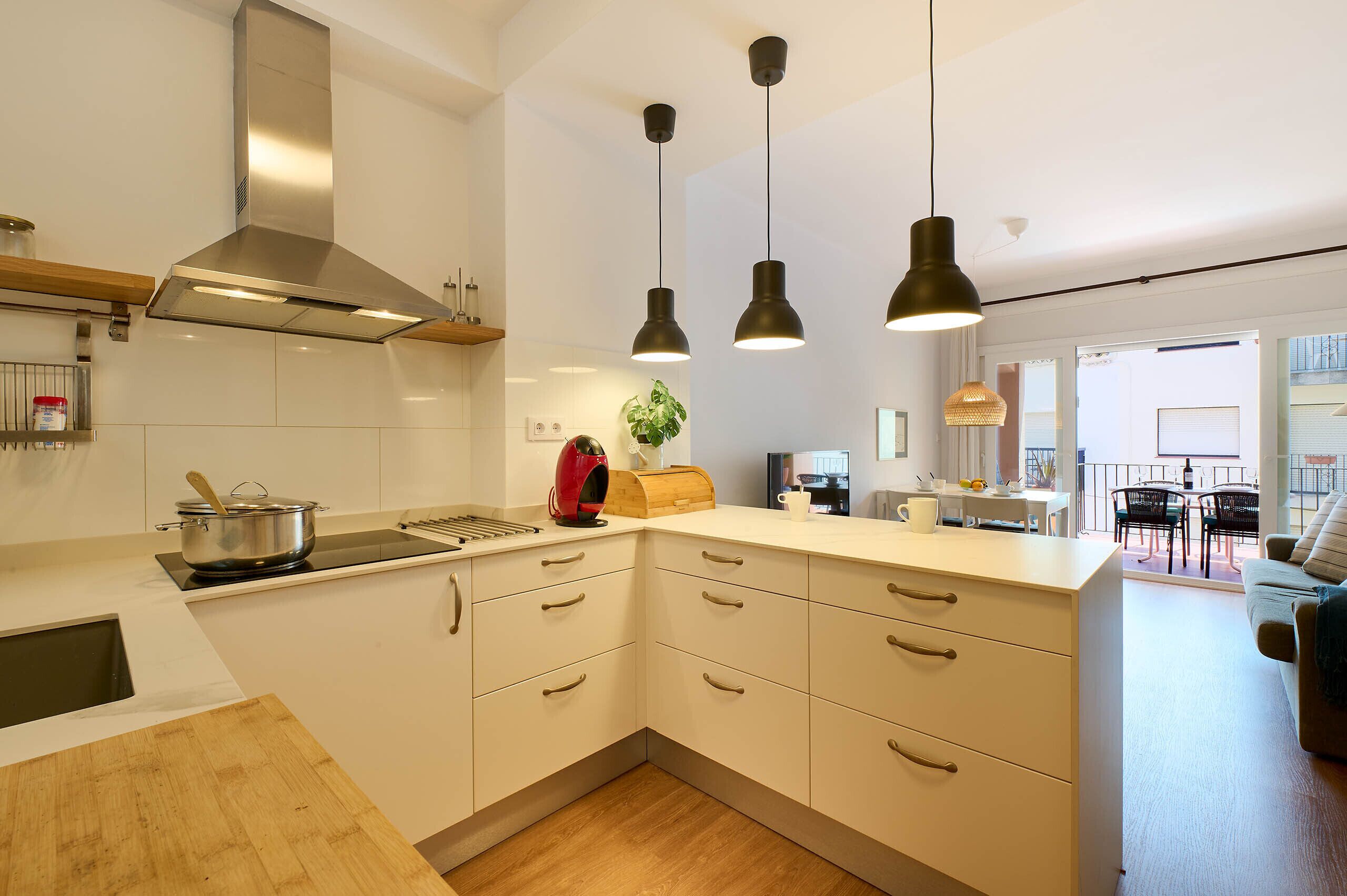 A modern kitchen with white cabinets, a stainless steel range hood, and pendant lighting.