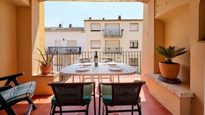 Eine Terrasse im Freien mit einem runden Esstisch, Korbstühlen, Topfpflanzen und Blick auf benachbarte Gebäude.