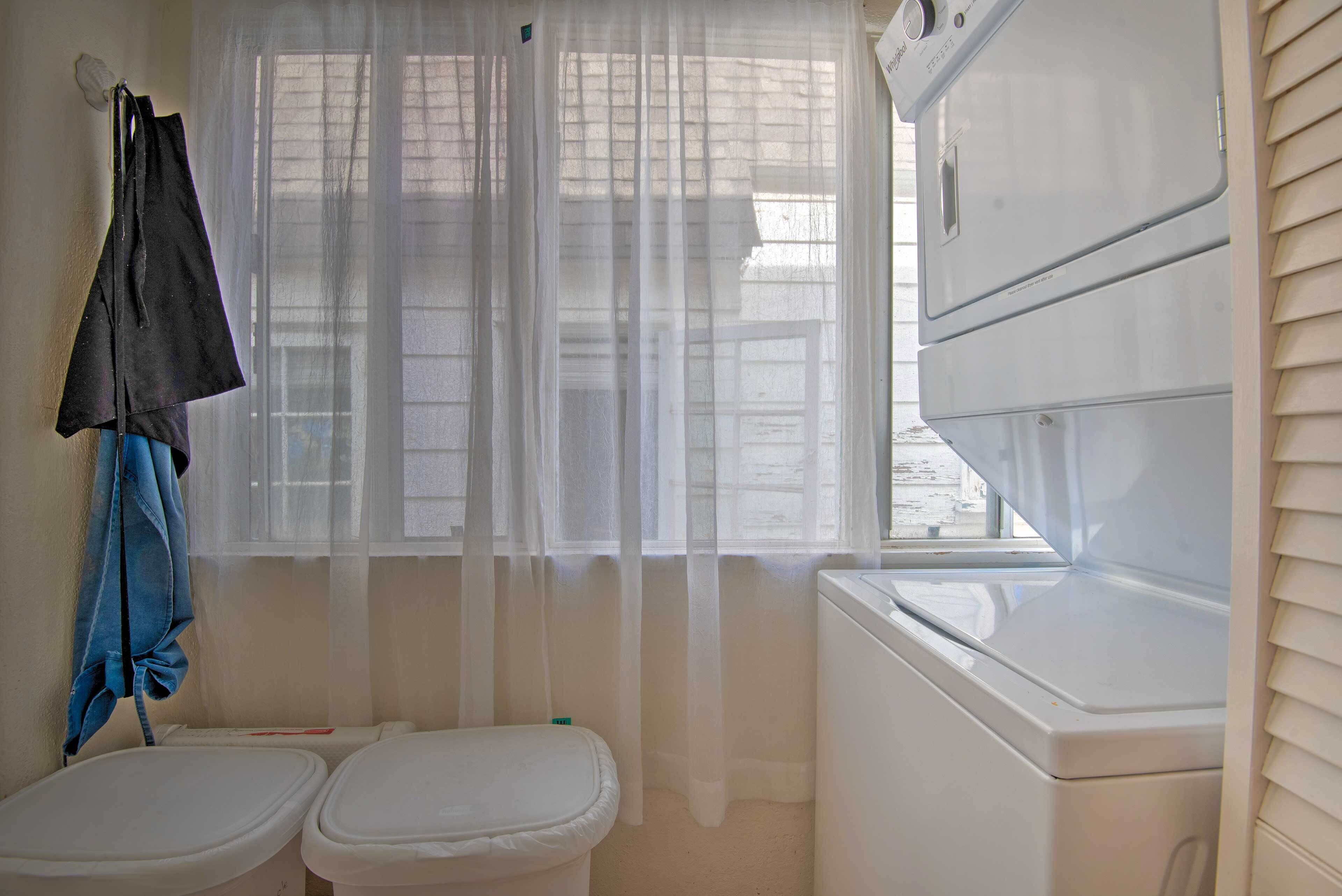 Un baño pequeño con dos inodoros, una lavadora y una ventana con cortinas translúcidas.