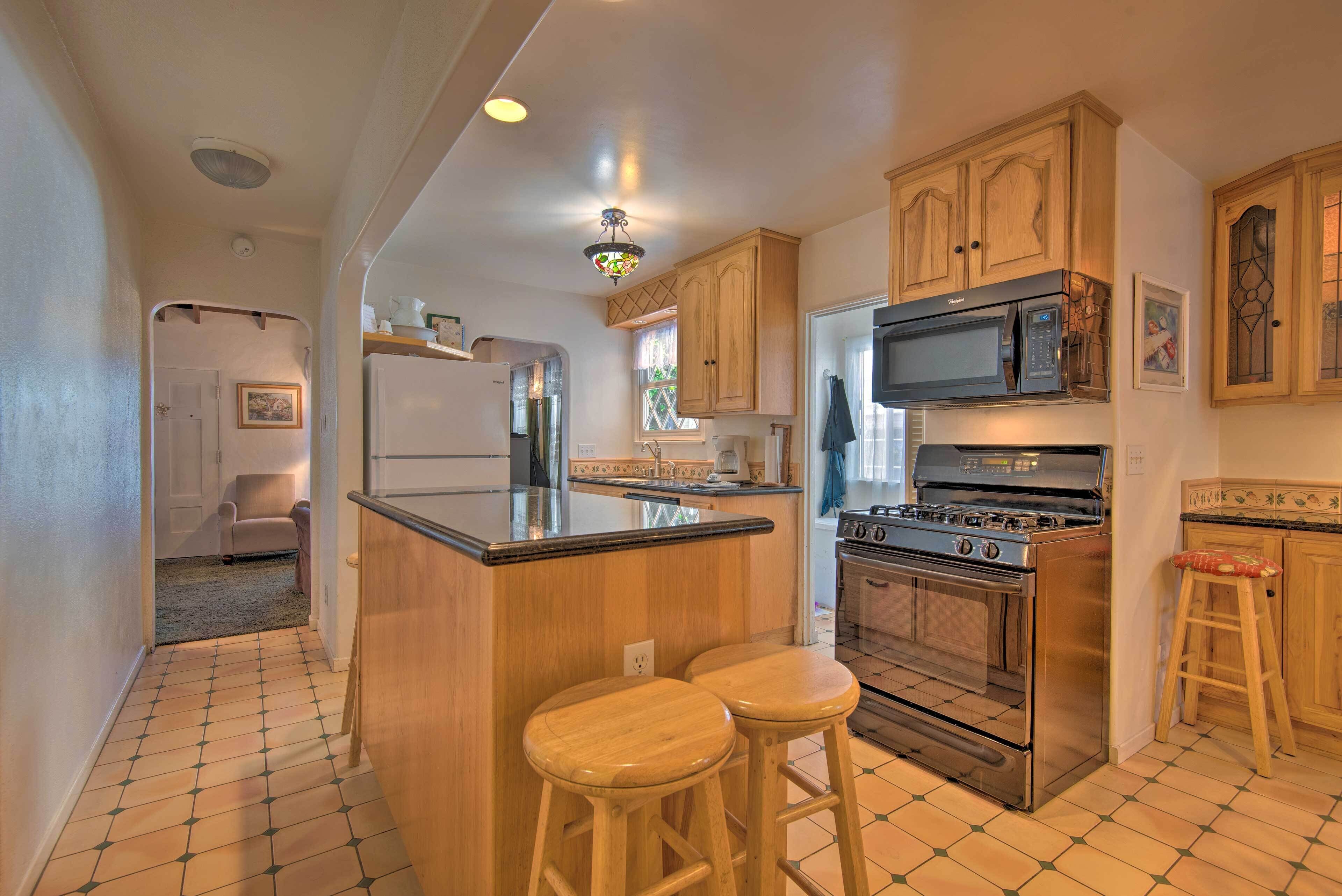 A kitchen with wooden cabinets, a central island with stools, a microwave, a stove, and a refrigerator.