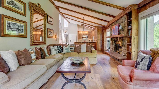 A spacious living room with a wooden ceiling, a large sofa, a coffee table, and a fireplace.