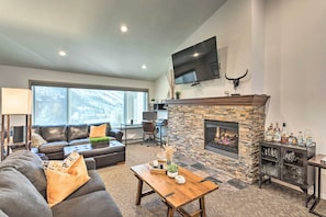 A modern living room with a stone fireplace, leather sofas, a flat-screen TV, and a large window.
