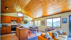 A spacious kitchen with wooden cabinets, a dining area with a table and chairs, and a cozy living room with a sofa and cushions. - The Atomic Squirrel Lodge Lake Gregory Getaway! (Crestline)