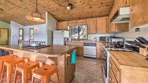 A kitchen with wooden cabinets, a central island with stools, a microwave, a toaster, and a dishwasher. - The Atomic Squirrel Lodge Lake Gregory Getaway! (Crestline)