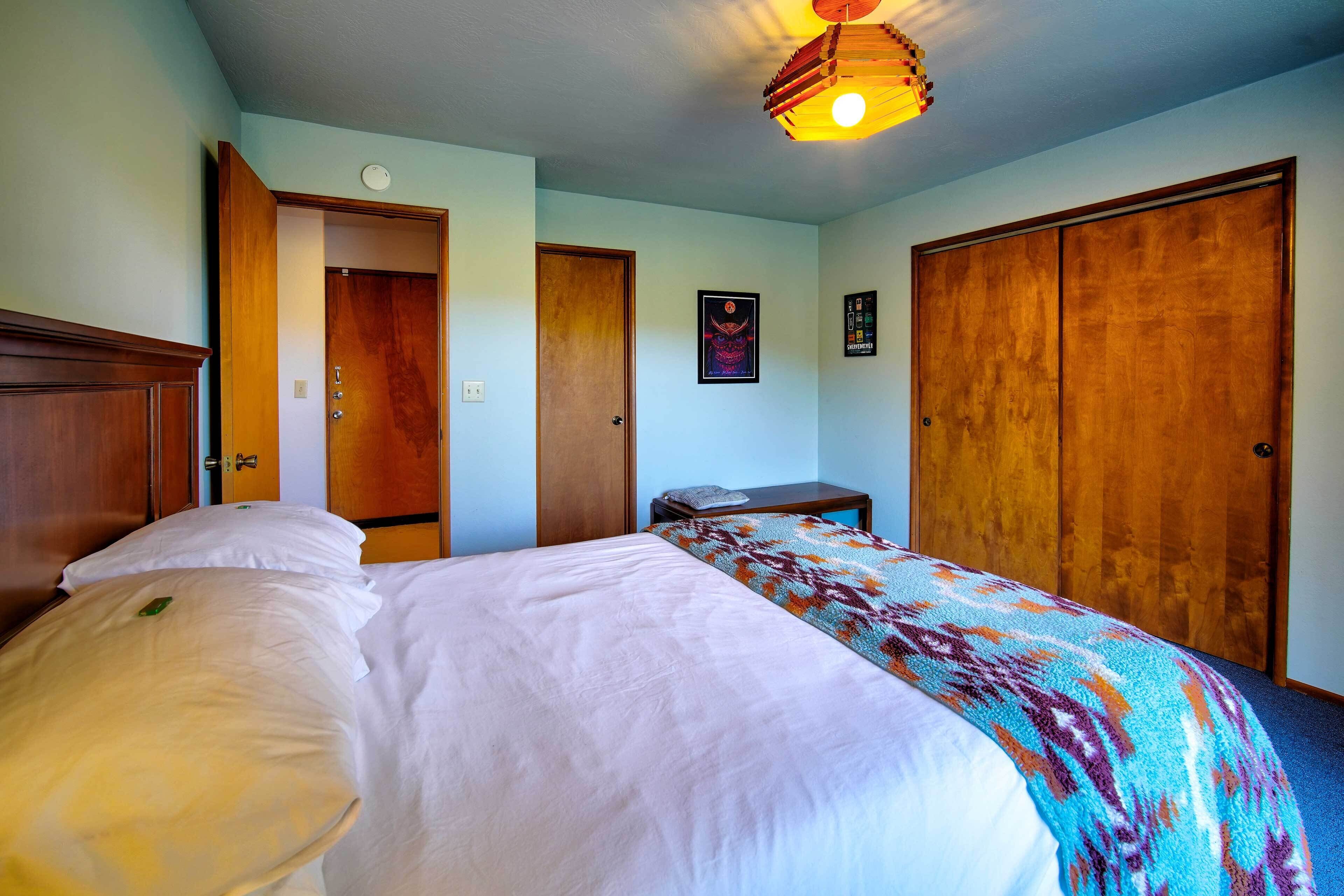 A bedroom with a bed, a wooden wardrobe, a nightstand, and a ceiling light fixture.