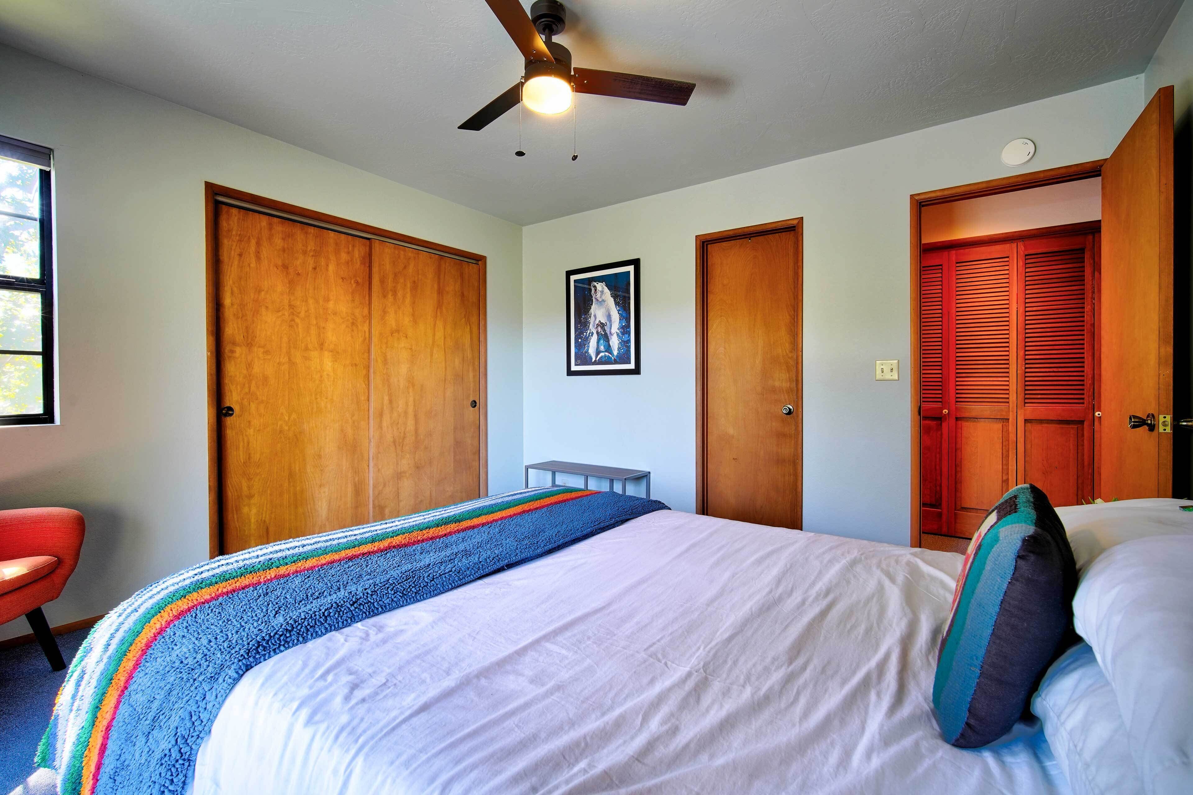 A bedroom with a bed, a ceiling fan, a window, and wooden doors.