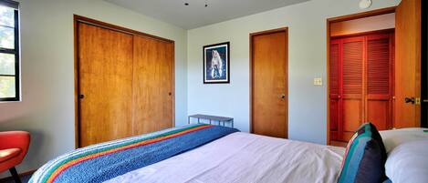 A bedroom with a bed, a ceiling fan, a window, and wooden doors.