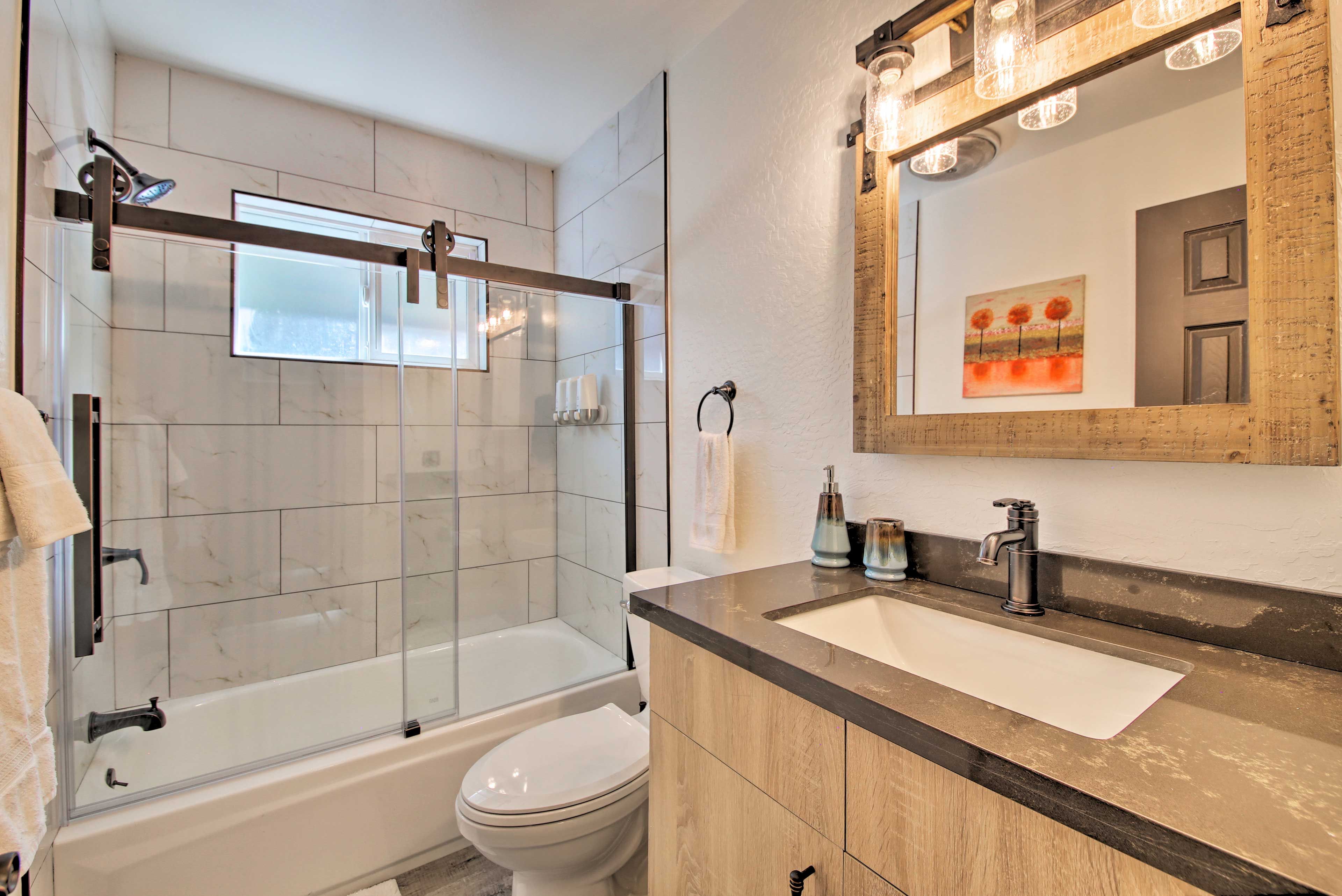 Un baño moderno con ducha de vidrio, inodoro blanco y tocador con un espejo grande y lavabo.