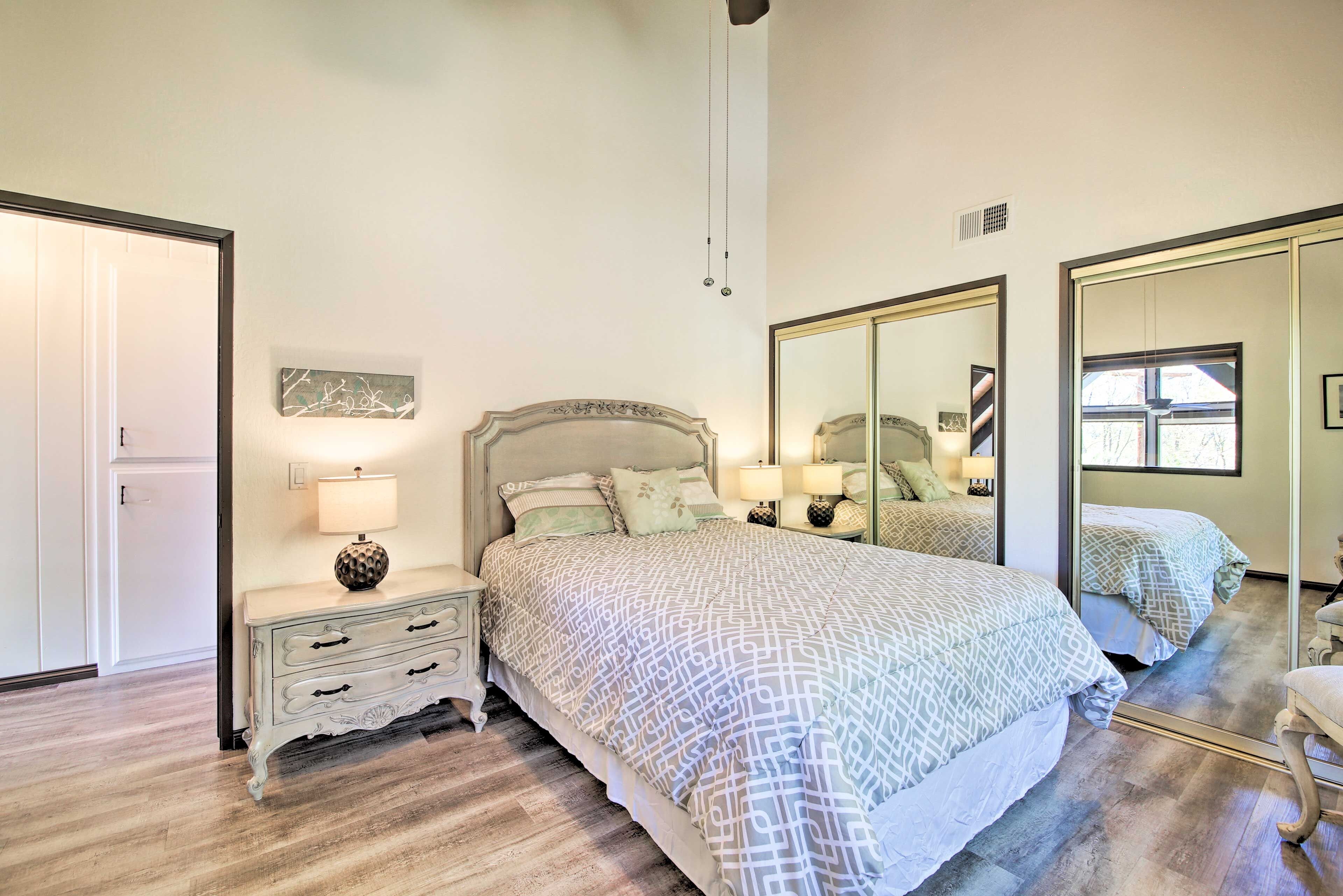 A bedroom with a large bed, a nightstand with a lamp, a dresser, and a mirror.