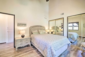 Quarto com uma cama grande, uma mesa de cabeceira com abajur, cômoda e espelho.